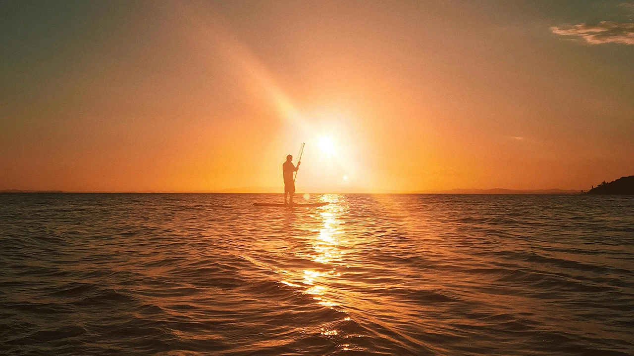 Silhouette of a paddleboarder at golden sunset on calm Maldives waters