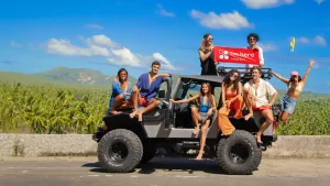 Imheretravels friends holding a banner on a jeep with a background of a tropical forest and mountains in Siargao