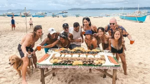 Group of friends on a table full of food such as seafoods, tropical fruits and rice portraying siargao and coconut trees